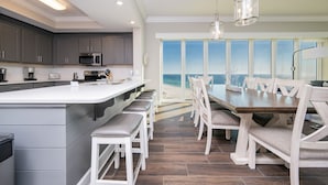 A modern kitchen with a large island, dark wood flooring, and a dining area with white chairs and a wooden table.