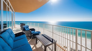 A balcony with a view of the ocean, furnished with blue sofas and a wooden table.