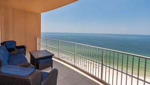 A balcony with wicker furniture, a small table, and a view of the ocean and beach.