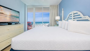 A hotel room with a large bed, a television, a ceiling fan, a view of the beach, and a white headboard. - Lighthouse 403 1 Bedroom Condo (Gulf Shores)