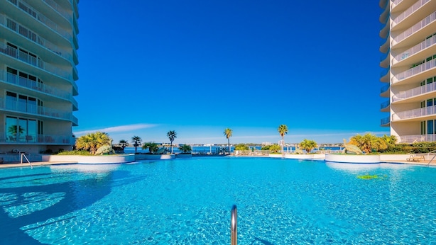 Una piscina amplia y cristalina rodeada de palmeras y edificios modernos con balcones.