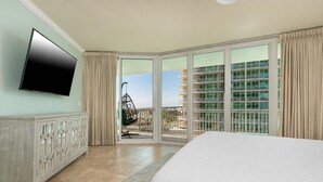 Habitación de hotel con cama, televisión, puerta corrediza al balcón y vista a un edificio.
