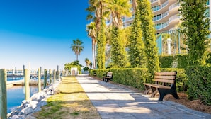 Un paseo marítimo con un banco, un muelle de madera y un edificio con balcones con vistas al agua.