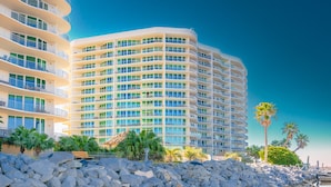 Un hotel de varios pisos con balcones, una costa rocosa y palmeras.