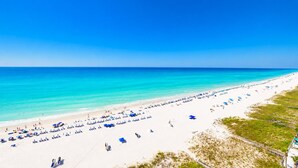 A beach with rows of sun loungers and umbrellas, a clear blue sky, and the ocean.
