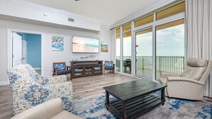A spacious living room with a large sliding glass door leading to a balcony, a wooden coffee table, and two armchairs.