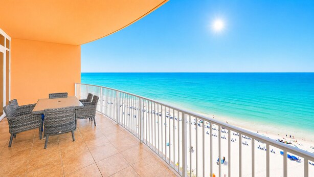 A balcony with a view of the beach, a table, and wicker chairs.