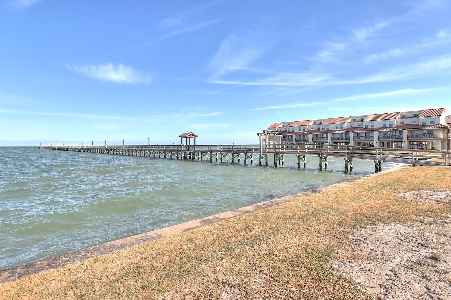 A coastal hotel with a long pier extending into the sea, featuring a gazebo and multiple balconies.