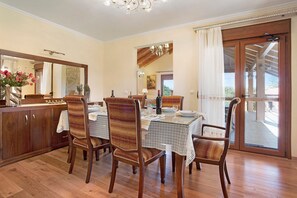 Un comedor con sillas de madera, una mesa con mantel de encaje, un armario de madera y un espejo grande.
