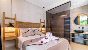 Een moderne hotelkamer met een groot bed, een houten hoofdeinde, nachtkastjes, een badkamer met douche, wastafel en spiegel.