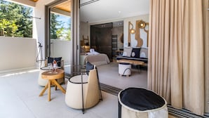 Een moderne hotelkamer met een glazen deur naar een balkon, een ronde tafel met een fles erop, een bank en een bed met hoofdeinde.