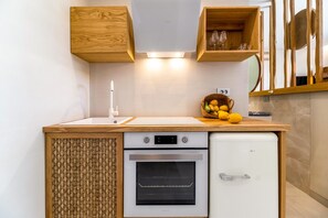 A compact kitchen with a built-in oven, a small refrigerator, wooden cabinets, and a basket of lemons on the counter.