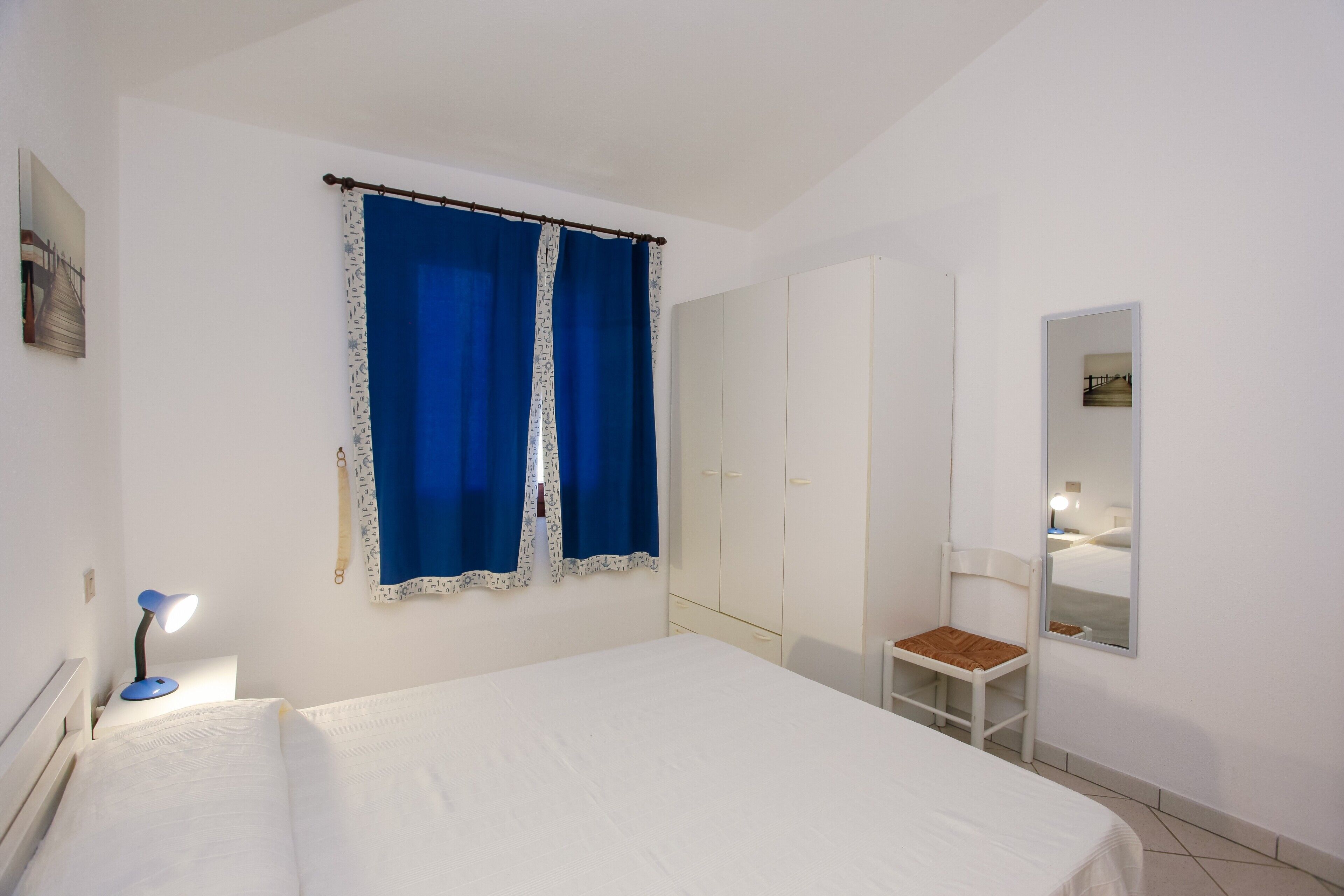 Une chambre à coucher avec un lit, un bureau avec une lampe, une chaise, une armoire et un miroir.