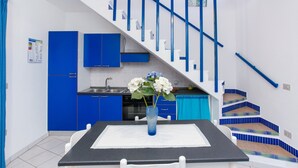 Eine moderne Küche mit blauen Schränken, einem Esstisch mit Blumenvase und einer Treppe mit blauen Geländern.