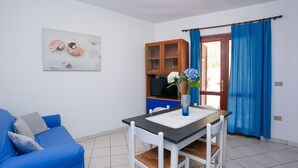 Ein Zimmer mit einem blauen Sofa, einem Esstisch mit Stühlen, einem Schrank, einer Vase mit Blumen und einem blauen Vorhang.