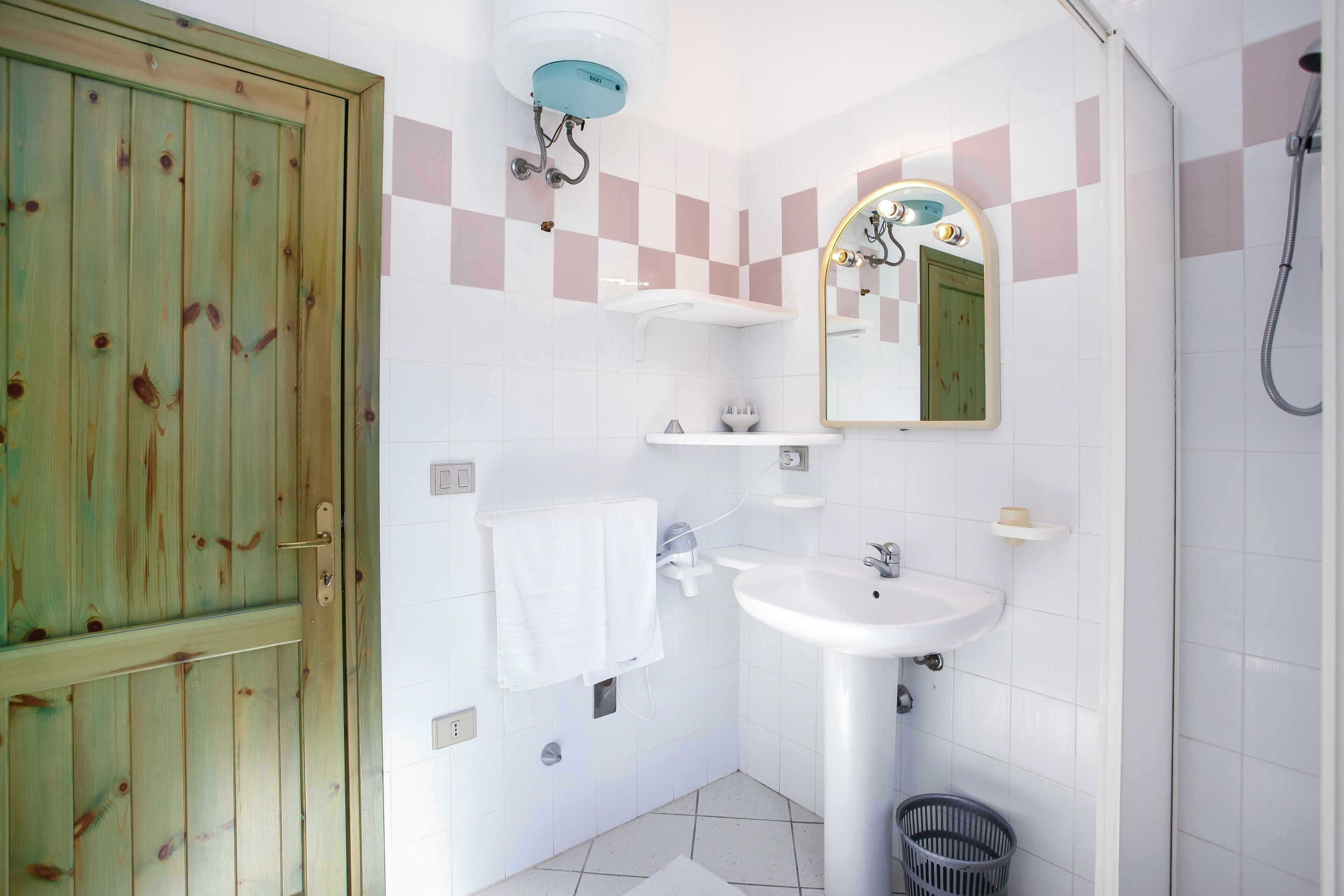 A bathroom with a wooden door, a sink, a mirror, and a shower.