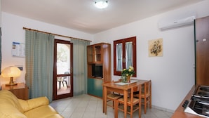 Un espacio habitable compacto con sofá, mesa de comedor, sillas, zona de cocina y un mueble pequeño.