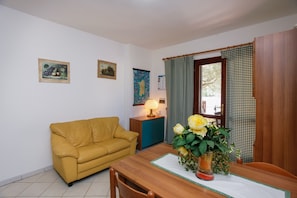 A yellow sofa, wooden dining table, and a vase with flowers.