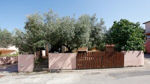 Una zona residencial cerrada con un camino de entrada pavimentado, un portón de madera y un árbol grande de follaje denso.