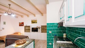 A kitchen with white cabinets, a green backsplash, and a dining area with a bed and a TV. - Holiday Home "mirtagru Bilo Mare 2" with Sea View, Private Terrace and Wi-Fi (Budoni)