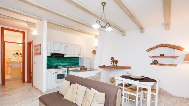 A cozy living room with a sofa, a dining table, and a kitchen area in the background. - Holiday Home "mirtagru Bilo Mare 2" with Sea View, Private Terrace and Wi-Fi (Budoni)