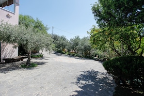 A paved courtyard with stone flooring, surrounded by trees and a building with a pink facade.