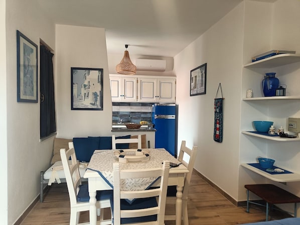 A compact kitchen with white cabinets, a blue refrigerator, and a dining area with a table and chairs.