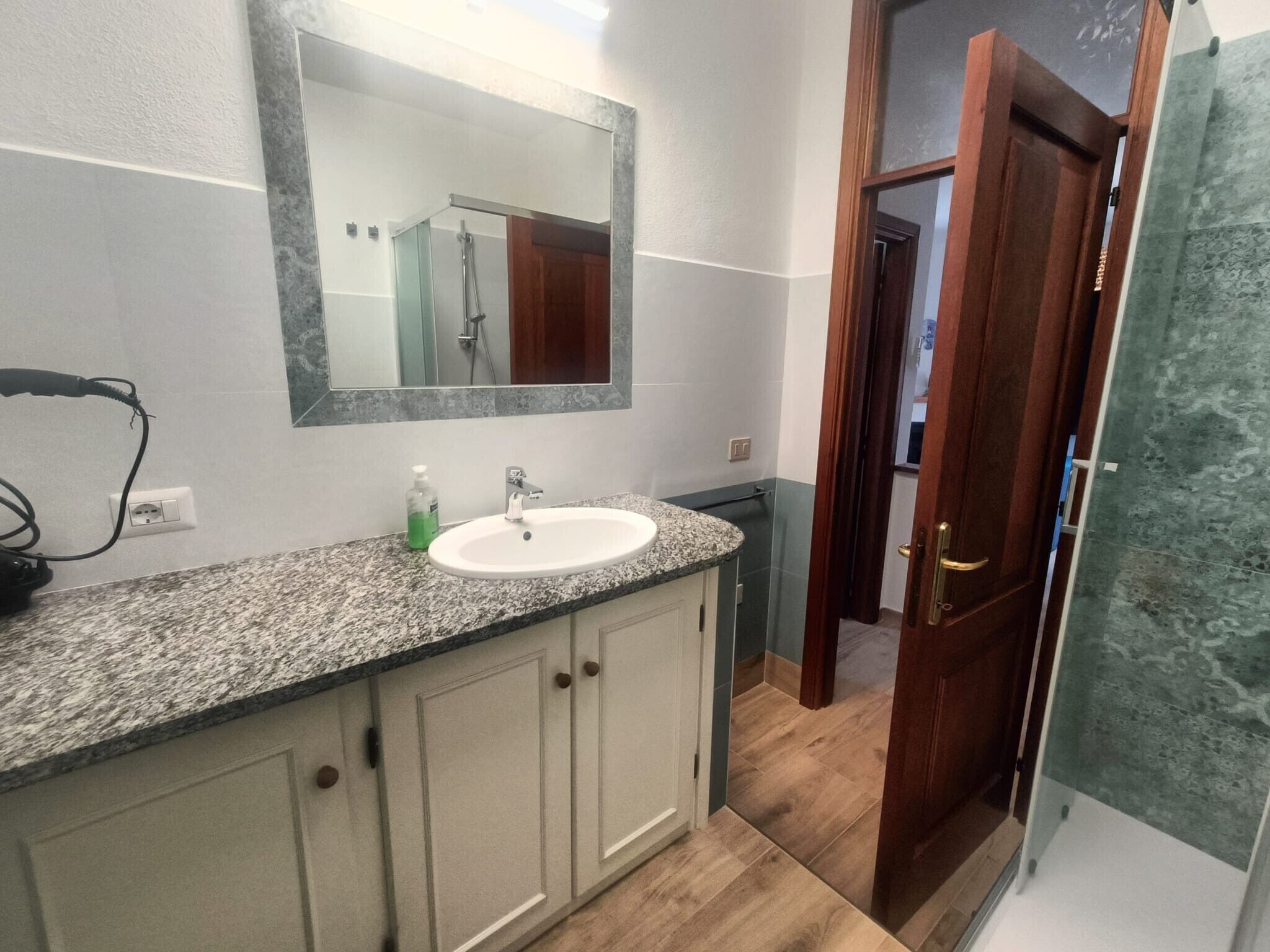 A bathroom with a granite countertop, a white sink, a mirror, and a shower area.