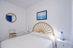 A bedroom with a bed, a nightstand, a chair, a bedside table, a lamp, a mirror, and a painting on the wall.