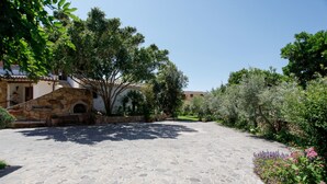 Ein gepflasterter Innenhof mit Steinplattenbelag, umgeben von Grünpflanzen und einem Gebäude mit einer steinernen Fassade.