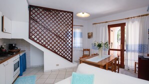 Una cocina con estufa, horno y pileta, un comedor con mesa y sillas, y una escalera con baranda de madera.