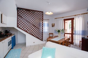 A kitchen with a stove, oven, and sink, a dining area with a table and chairs, and a staircase with a wooden railing.
