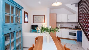 Un comedor con una mesa de madera, sillas, un florero con flores, un armario azul y una cocina al fondo.