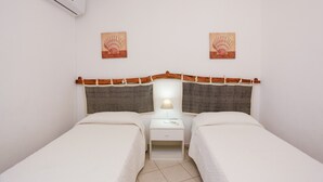 Una habitación con dos camas, una mesita de noche con lámpara y un equipo de aire acondicionado.