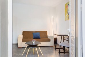 Un salon moderne comprenant un canapé, une petite table ronde avec un vase, un fauteuil et un bureau avec une chaise.