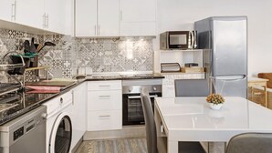 Een moderne keuken met witte kastjes, een roestvrijstalen koelkast, een magnetron en een inbouwoven.