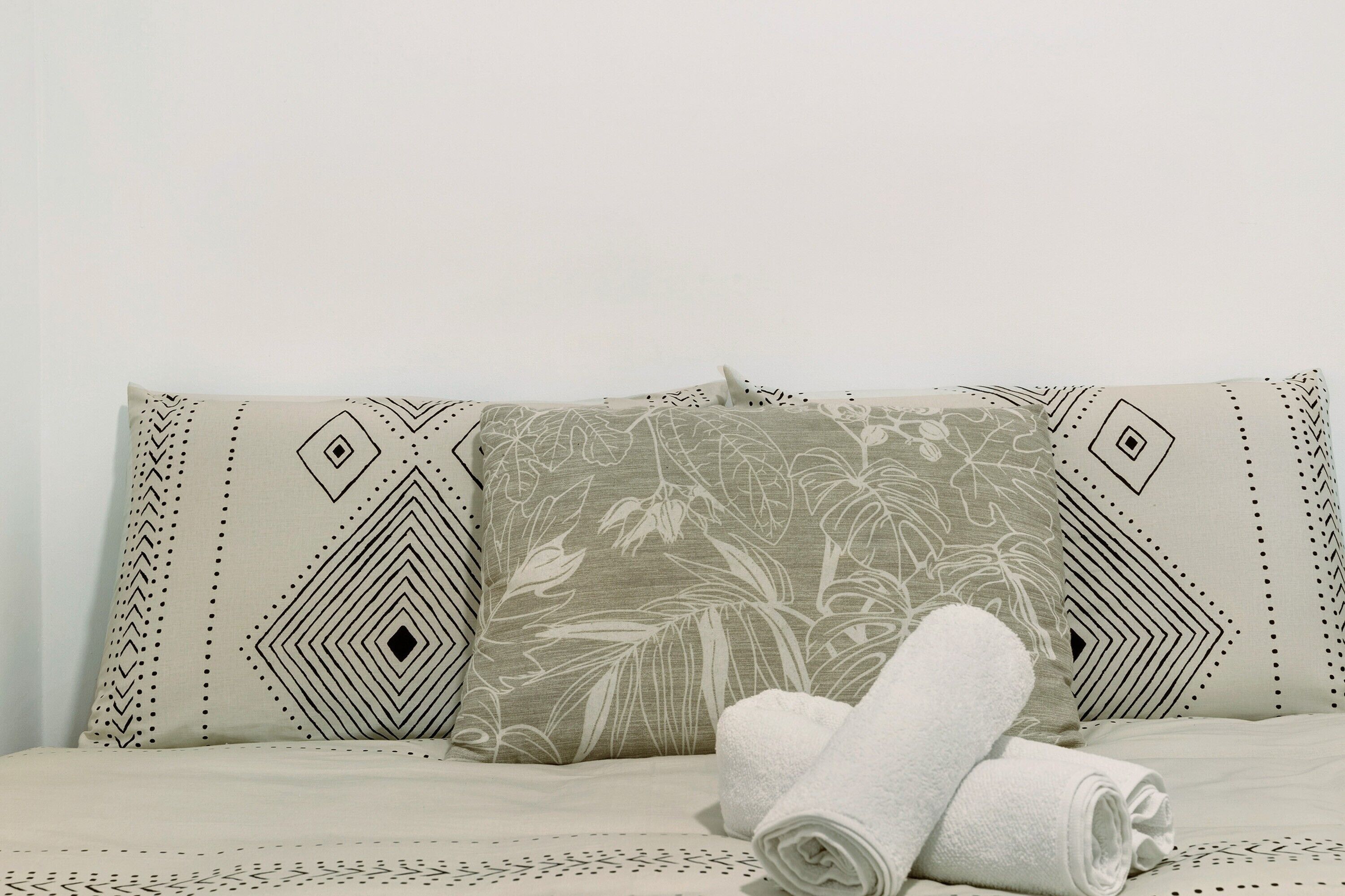 Una cama con almohadas estampadas y toallas enrolladas.