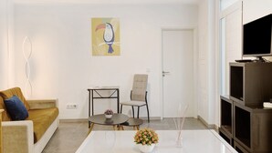 Een woonkamer met een bank, een stoel, een bijzettafeltje, een televisie en een schilderij aan de muur.