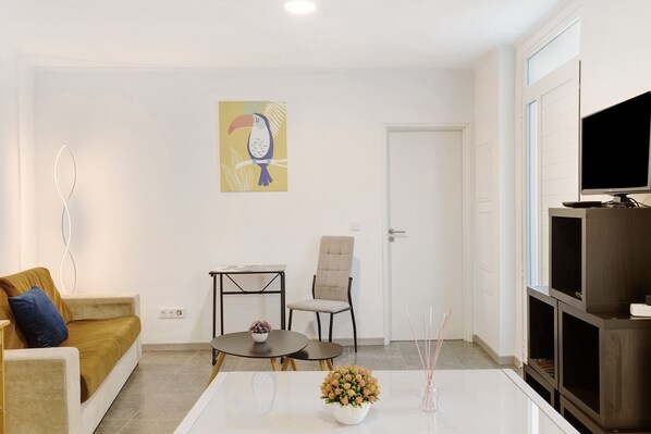 Una sala de estar con un sofá, un sillón, una mesita, un televisor y un cuadro en la pared.