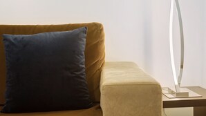 Een bank met een kussen, een klein poufje en een moderne vloerlamp.