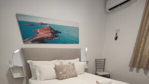 Een netjes opgemaakt bed met witte lakens, een hoofdbord en daarboven een schilderij van een kustlandschap.