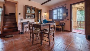 A dining area with a wooden table and chairs, a staircase, a bookshelf, and a window with a view of the outside.