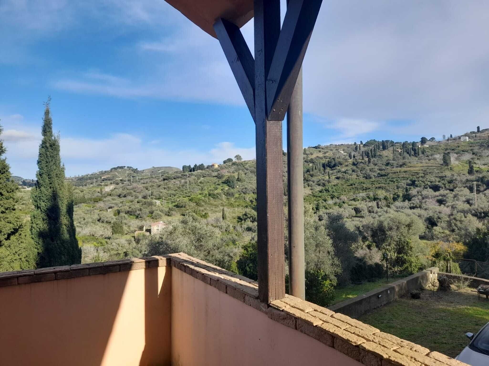 Un balcón con vistas a un paisaje montañoso, vigas de madera y un muro de ladrillo.