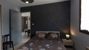 A bedroom with a bed, bedside table, lamp, and a door leading to a dining area. - Holiday Home "Ombre d'Été" with Private Garden & A/C (RUOMS)
