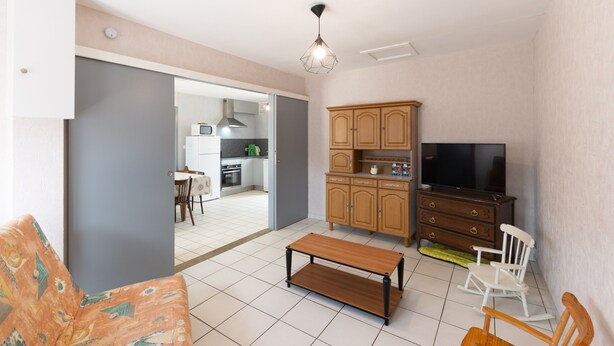 A living room with a sofa, a wooden coffee table, a TV, and a kitchen in the background. - Holiday Home "Ombre d'Été" with Private Garden & A/C (RUOMS)