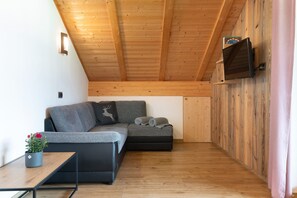 Un intérieur moderne avec un plafond en bois, un canapé gris, une petite table sur laquelle est posée une plante en pot et un téléviseur fixé au mur.