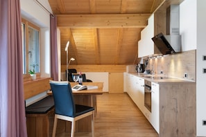 Une cuisine moderne avec des poutres en bois, un coin repas avec une table et des chaises, et une fenêtre avec des rideaux.