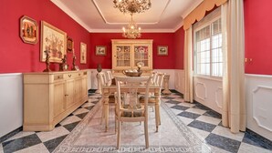 Een eetkamer met een zwart-wit betegelde vloer, een kroonluchter, een eettafel met stoelen en een kast met glazen deuren.