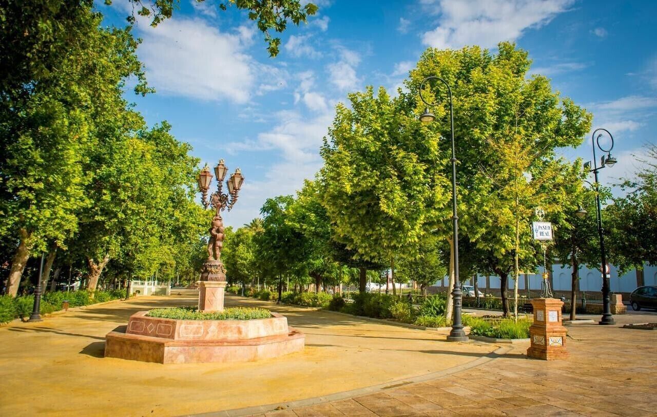 Un parque con una estatua, árboles y un camino pavimentado.