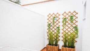 Una esquina de una habitación con una pared blanca, un adorno de pared de madera celosía y dos plantas en macetas.